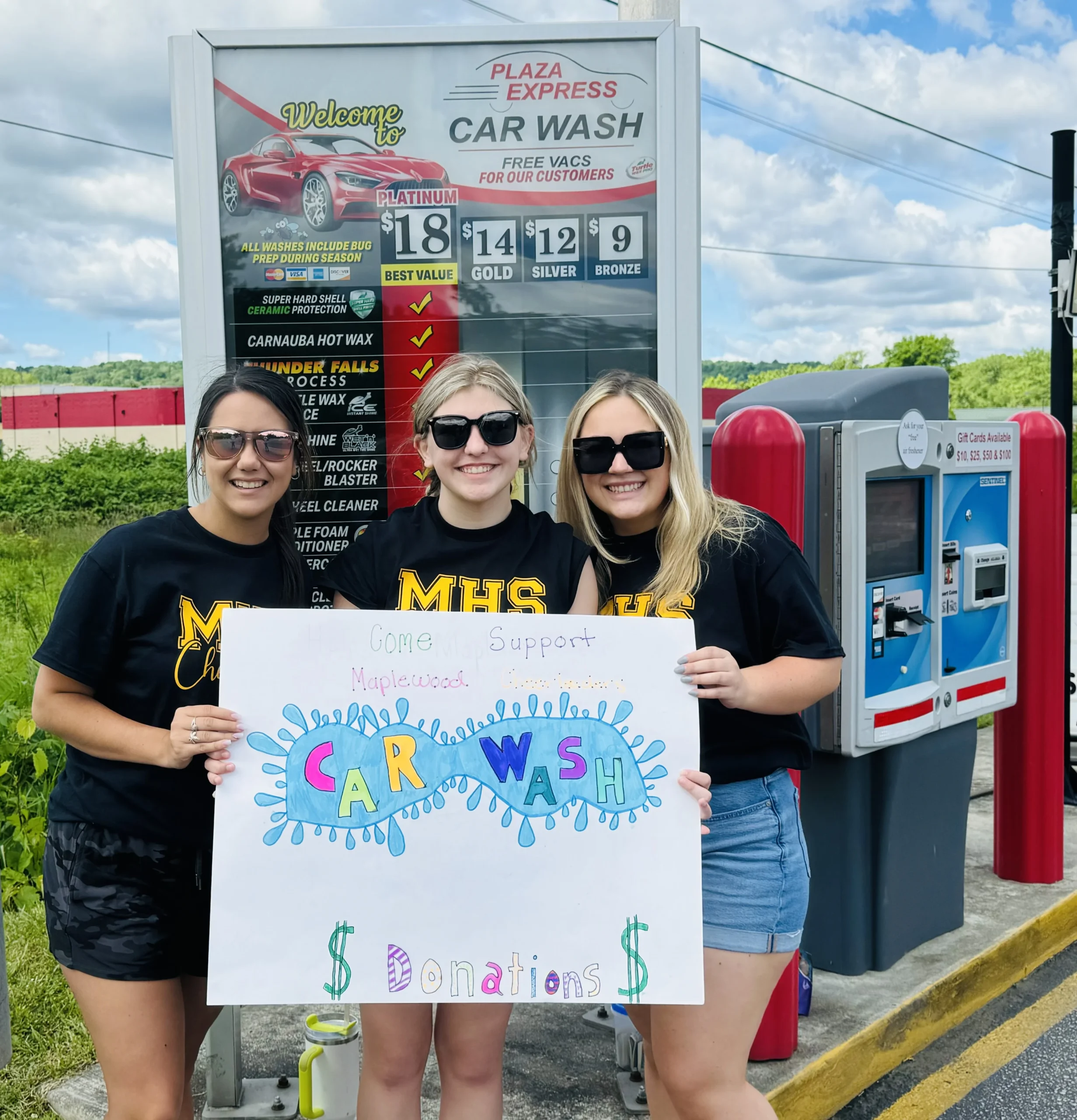 Three women holding a sign in front of a gas station.